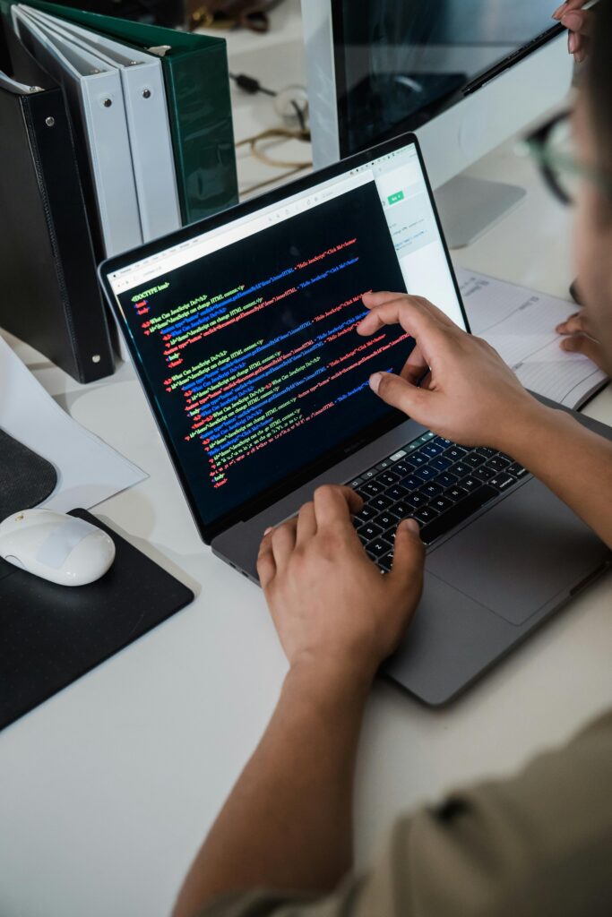 pexels photo 12899188 12899188 Close-up of a programmer pointing at a colorful code script on a laptop in an office setting.